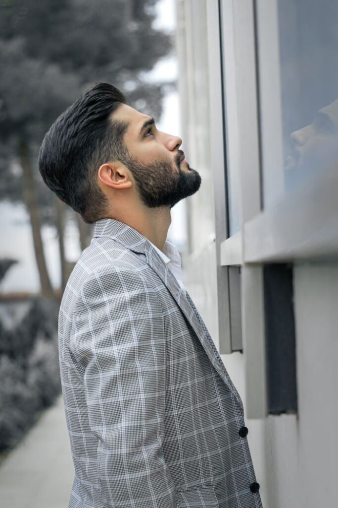 Elegant businessman in gray suit with well-groomed beard looking up outdoors.